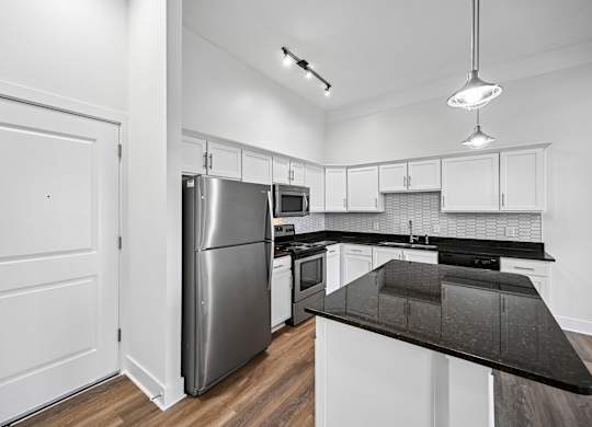 A modern kitchen with a stainless steel refrigerator and black countertops.