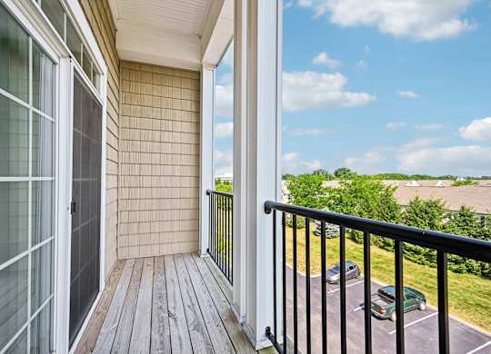 A balcony with a black railing and a view of a parking lot and trees.