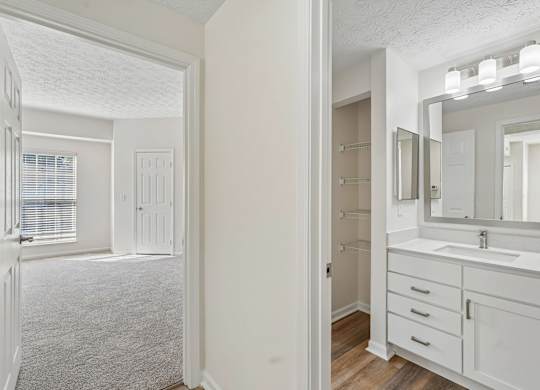 A white bathroom with a sink, mirror, and wooden floors.