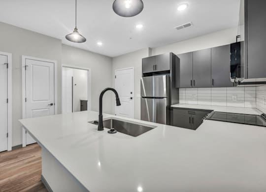 A modern kitchen with a long white countertop and stainless steel appliances.