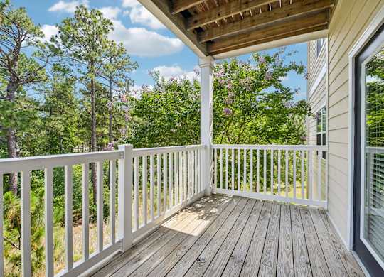 A wooden deck with a white railing and a view of trees.