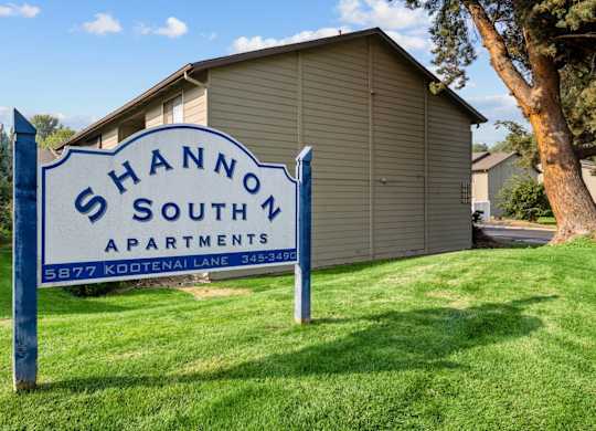 A blue and white sign that says Shannon South Apartments stands in the grass in front of a building.