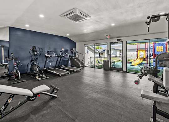 Fitness center with treadmills and glass doors to playground at Peaks at Live Oak Apartments, San Antonio, Texas