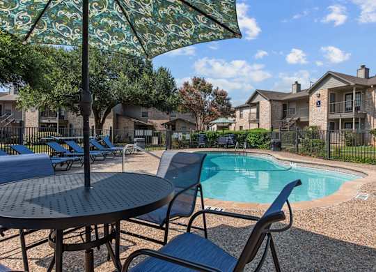 Pool area with patio furniture and decorative umbrella at Peaks at Universal City Apartments, Universal City, Texas