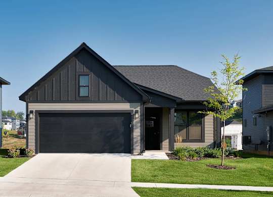 A modern house with a garage door and a tree in front.