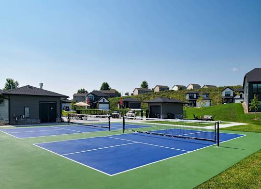 A tennis court with a green and blue surface is surrounded by houses.