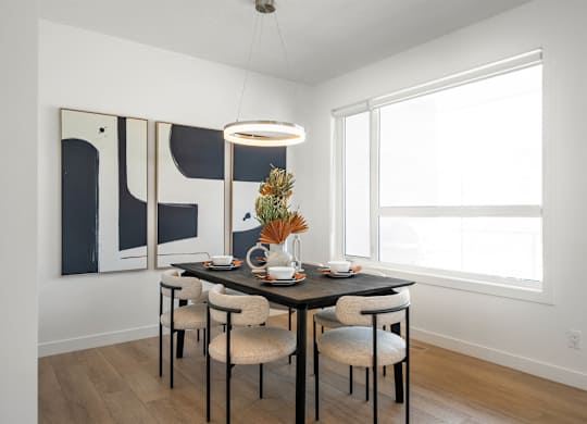 A dining room with a table set for two and a modern art piece on the wall.