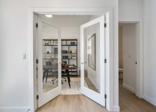 A white door opens to a room with a desk and chairs.