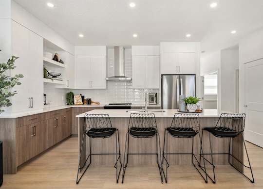 A modern kitchen with a bar area and three black chairs.