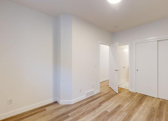 A room with white walls and wooden flooring with a door on the right.