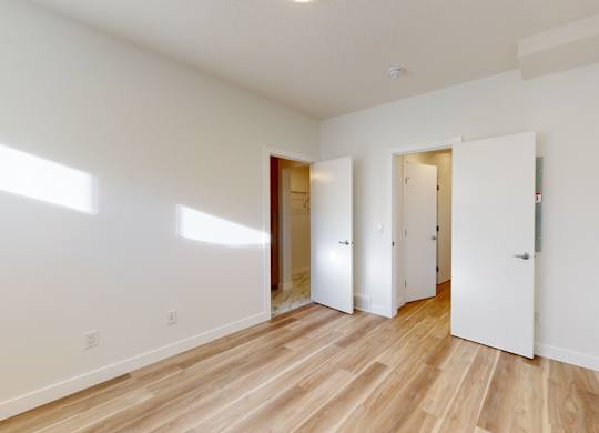 A room with white walls and wooden flooring with three doors.