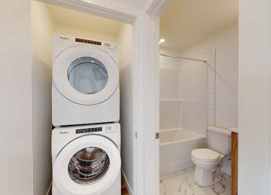 A white washing machine and dryer stacked on top of each other in a small laundry room.