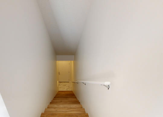 A long hallway with a wooden staircase leading to a door at the end.