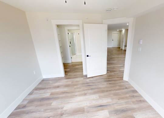 A room with white walls and wooden flooring with two open doors.