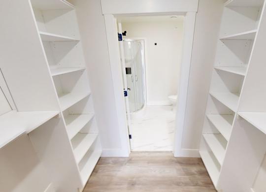 A hallway with white shelves on both sides leading to a door.