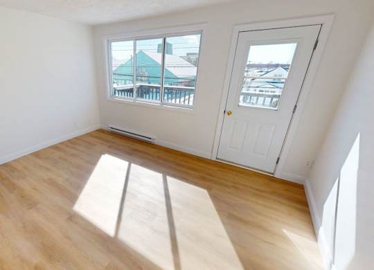 A room with a white door and a window with a view of a green building.