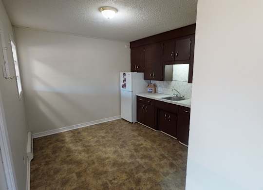 A kitchen area with a refrigerator, sink, and cabinets.