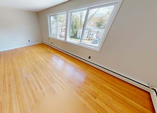 A room with wooden flooring and a window overlooking a residential area.