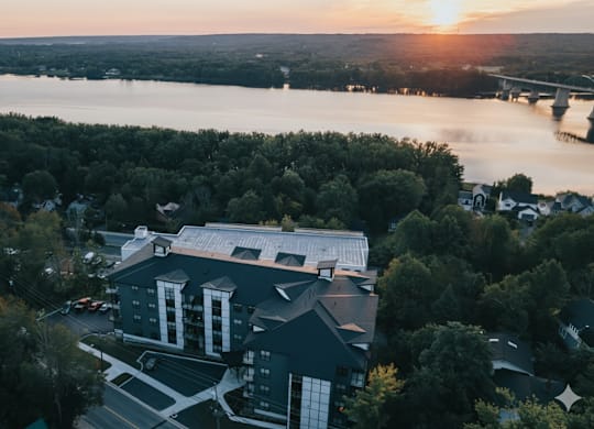 A large building with a white roof is surrounded by trees and overlooks a body of water.