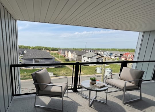 A balcony with two chairs and a table overlooking a residential area.
