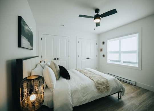 A bedroom with a bed, pillows, a lamp, and a ceiling fan.