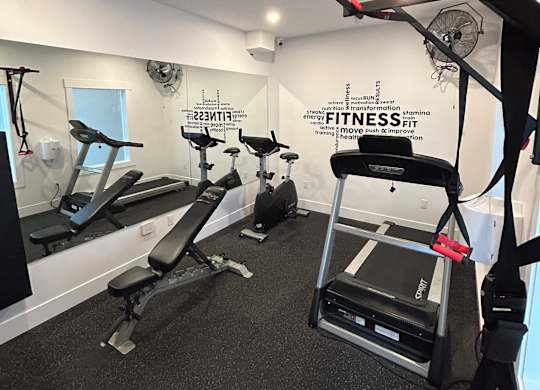 A gym with a variety of equipment including a treadmill, a stationary bike, and a rowing machine.