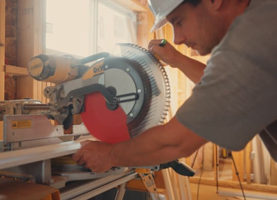 A man in a hard hat is using a circular saw to cut a piece of wood.