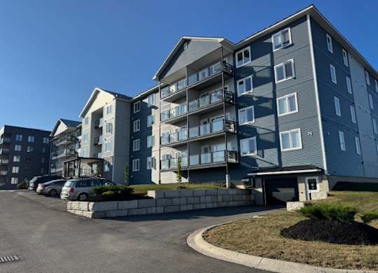 Apartment complex with grey and blue buildings and cars parked in the driveway.