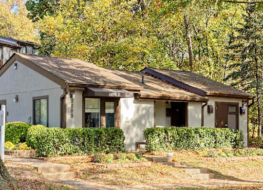 A house with a white facade and a brown roof is surrounded by greenery.