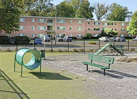 A dog park with a green slide and bench in front of a brick building.