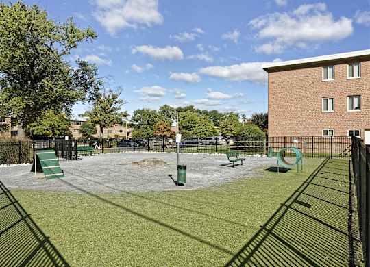 A dog park with a green slide and a brown building in the background.