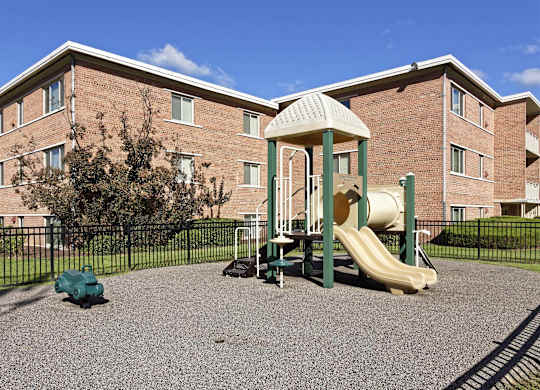 A playground with a slide and a tree in front of a brick building.