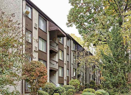 A building with a brown and beige exterior is surrounded by trees and bushes.