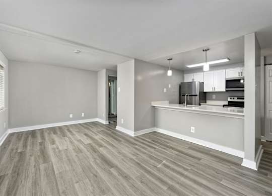A spacious living room with a wood floor and a kitchen area in the background.