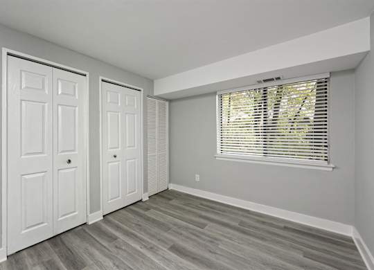 A room with two white doors and a window with blinds.