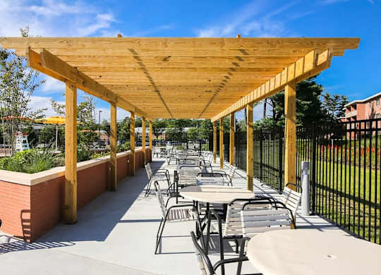 A wooden pergola with tables and chairs is set up on a patio.