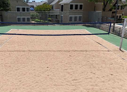 A sand volleyball court with a green fence around it.