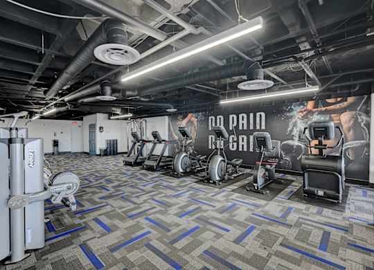 A gym with a variety of equipment including a rowing machine, a treadmill, and a weight bench.