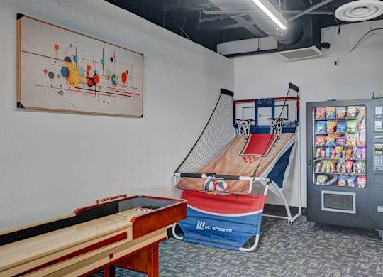 A room with a pool table, a basketball hoop, and a vending machine.