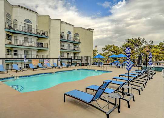 A pool area with sun loungers and umbrellas in front of a building.