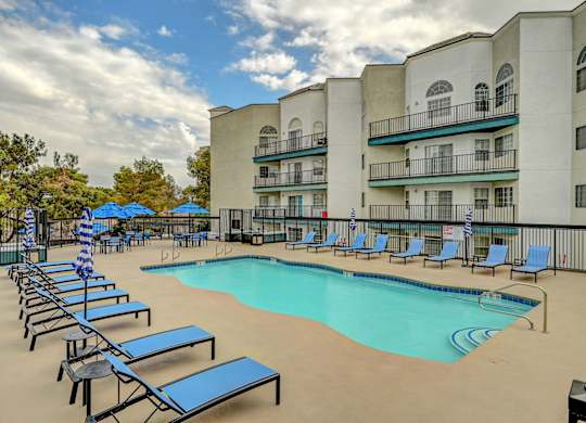 A swimming pool surrounded by sun loungers and apartment buildings.