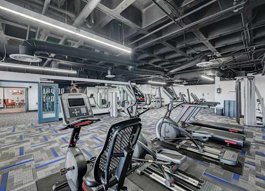 A gym with a variety of exercise equipment including treadmills, stationary bikes, and elliptical machines.