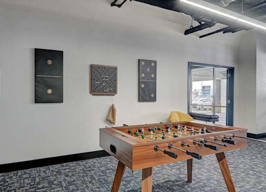 A foosball table is in the middle of a room with a white wall and a window.