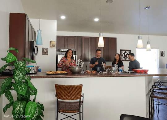 A group of people are gathered around a kitchen island with food and drinks on it.