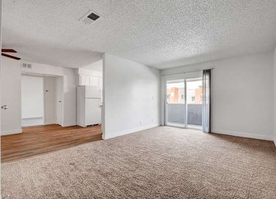 A spacious room with a carpeted floor and a sliding glass door leading to a balcony.