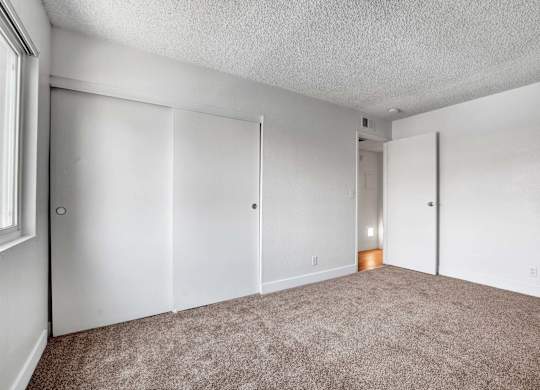 A room with carpeted floor and white walls with a door on the left.