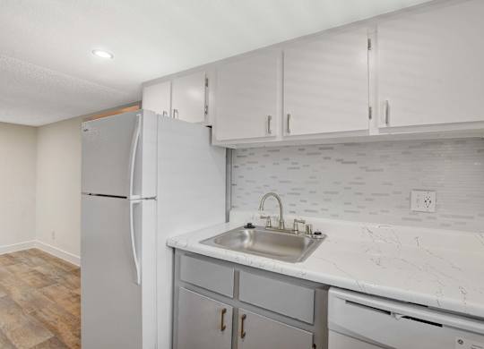 A kitchen with a white refrigerator, marble countertops, and wooden flooring.