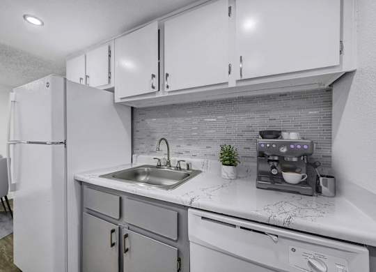 A modern kitchen with a white refrigerator, grey cabinets, and a marble countertop.
