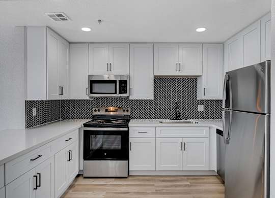 A kitchen with white cabinets and a black and white backsplash.
