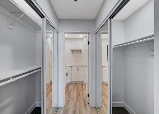 A hallway with white walls and wood floors leading to a kitchen.